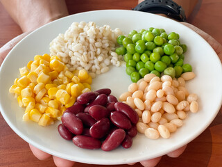 top view of navy bean and red bean and corn and  green peas and millet in white plate on hand - 508565716