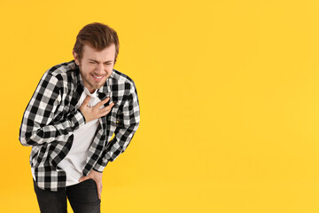 Young man with pain on yellow background