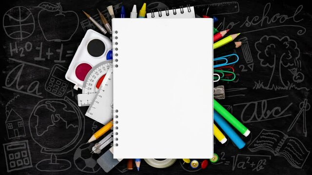 Colorful school supplies being moved underneath the blank notepad. School and Education concept. Blackboard and chalk icon background. Seamless looping. High quality 4k video.