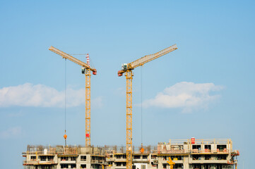 Two large yellow industrial cranes operating on an apartment house construction site