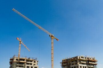 Two large yellow industrial cranes operating on an apartment house construction site
