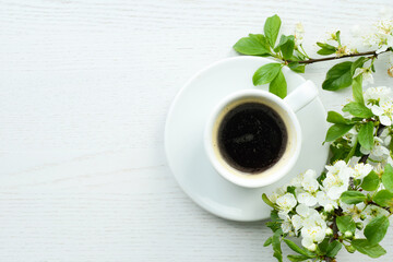 Coffee and apple tree flowers. Black hot coffee in a white coffee cup and a blooming apple tree branch on a white wooden background or table