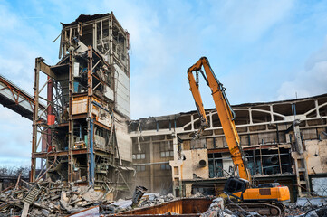 Fototapeta na wymiar Disassembling of old industrial building by high excavator