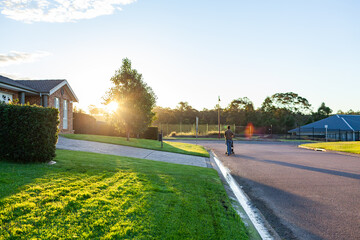 Person pushing pram down suburban street at sunset