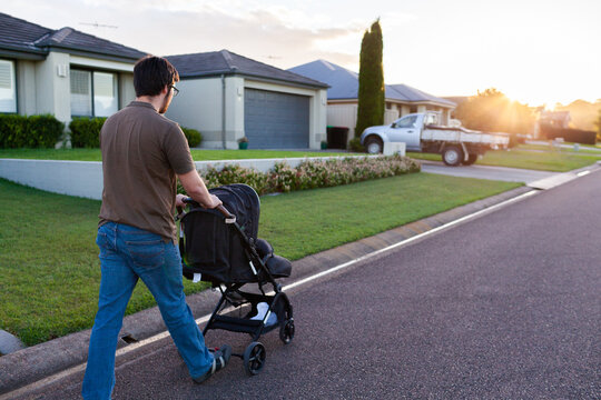 Young parent pushing baby in pram down road at sunset