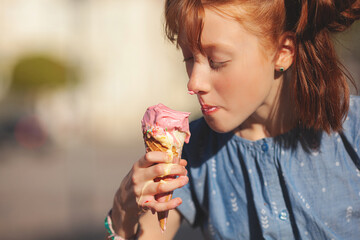 Cute girl eating ice cream on summer background outdoors. closeup portrait of adorable redhaired...