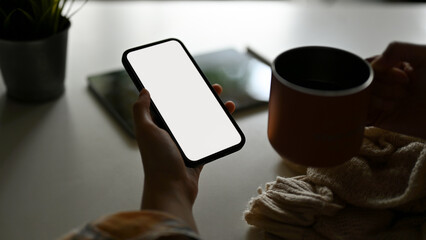 Close-up image, Relaxed female sipping morning coffee and using smartphone