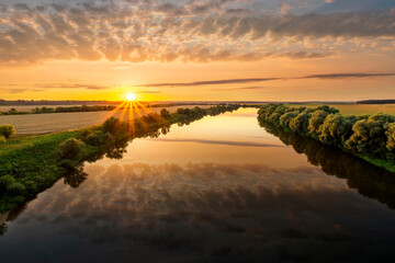 Amazing view at scenic landscape on a beautiful river and colorful sunset with reflection on water surface and glow on a background, spring season landscape