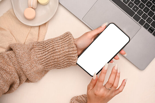 Overhead, Female in cozy sweater using smartphone at her minimal office desk.