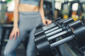 Fototapeta na wymiar Close up of a blurred caucasian woman selecting one of black dumbbell weight at gym. Healthy lifestyle concept. High quality photo