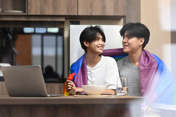 Romantic young gay couple embracing under LGBTQ pride flag. LGBT, pride, relationships and equality concept