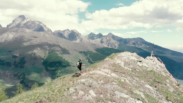 Aerial: Backpacker alpinist hiking to the mountain top, rocky mountain peak dramatic landscape. Summer adventures on the Alps. Conquering success leader concept