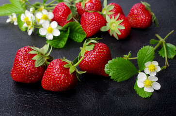Ripe strawberries with flowers and leaves on a black table.