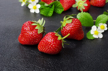 Ripe strawberries with flowers and leaves on a black table.
