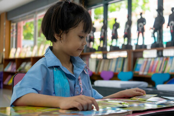 A girl student sitting in the library reading a book.