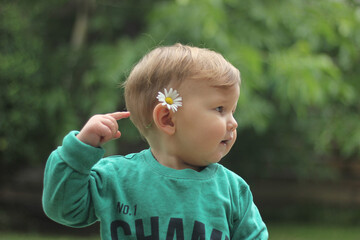 closeup face of funny teenage boy with freckles and camomile behind his ear on sunny grass background