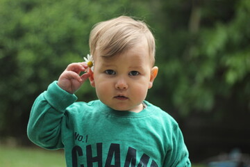 closeup face of funny teenage boy with freckles and camomile behind his ear on sunny grass background