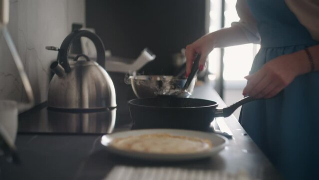 woman is cooking breakfast for family in sunday morning, housewife in blue apron is frying pancakes