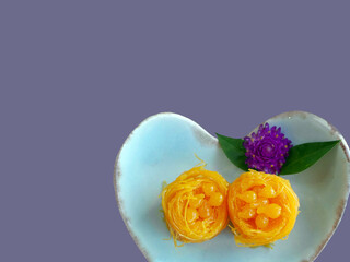 Top view Close up of Thai style Fios de ovos, rolled golden egg yolk thread, traditional sweet food dessert in blue heart shape plate, cut out isolated with copy space