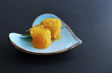 Close up of Thai style Fios de ovos, rolled golden egg yolk thread, traditional sweet food dessert in blue heart shape plate, with copy space