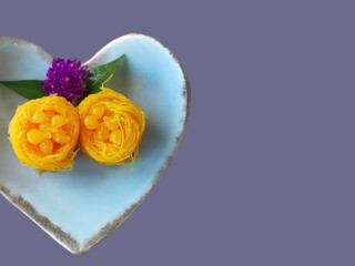 Top view Close up of Thai style Fios de ovos, rolled golden egg yolk thread, traditional sweet food dessert in blue heart shape plate, copy space with clipping path
