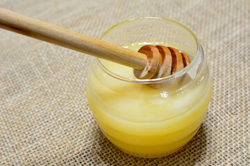 jar with honey and wooden honey stick on sack texture background