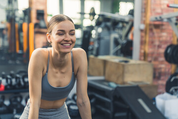 Medium indoor shot at a gym. Joyful fulfilled european woman in her 20s in a sports bra and leggings looking ahead and smiling after a training. High quality photo