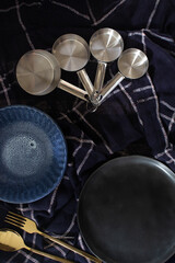 Dark kitchen concept, set of measuring spoon, empty plate and gold fork, blue textured cloth background.