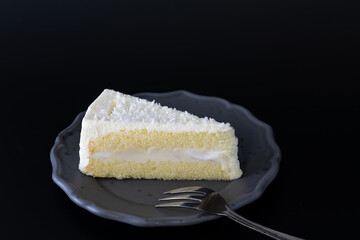 Sliced of coconut cake on dish with fork, dark moody concept, on dark background.