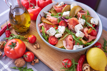 Salad with jamon or prosciutto, pears, tomatoes and arugula on wooden board