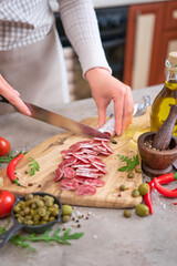 Woman slicing Spanish sausage fuet salami with knife on a domestic kitchen