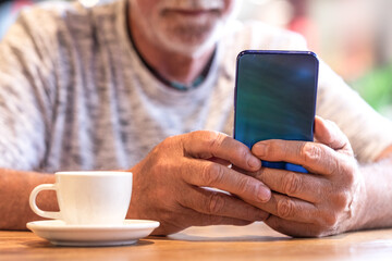 Cropped shot of a handsome senior man checking message on mobile phone while drinking coffee at cafeteria. Man using a smart phone while drinking espresso coffee