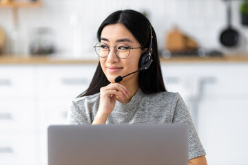 Asian female call center agent with headset working remotely from home on support hotline. Portrait...