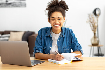 African American woman freelancer working from home. Happy female student using laptop computer, studying, distance learning or online education, looking at the camera smiling friendly