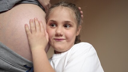 pregnant woman close-up belly. a little girl hugs her mother belly. happy family baby pregnancy newborn concept. daughter listening to pregnant mother belly. happy family expecting newborn baby