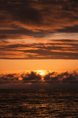 Beautiful magical enchanting sunset in orange tones with curly clouds on the sea. Amazing seascape. Horizon is above the water. Vertical photo