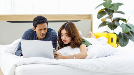 Fototapeta premium Asian upset stressed depressed frowning face male female husband and wife couple lay down together on pillow under blanket on bed having debt problem making payment shopping online via credit card