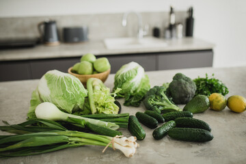 Still life with green fruit and vegetables on grey table in the kitchen interior.