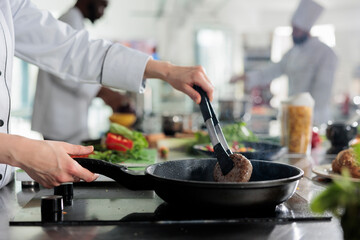 Master chef hands cooking beef patty in hot pan while cooking gourmet dish for dinner service. Skilled food industry worker frying minced meat in restaurant professional kitchen.