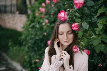 Young woman wearing pink dress enjoying fragrance of blooming roses in a spring garden.