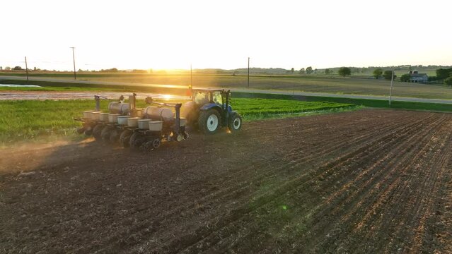 Drone view of tractor pulling seeder. Springtime planting in rural America. Golden hour sunlight reflects of tractor. Rotation into dust from dirt.