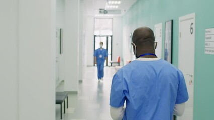 Male nurse with surgical mask walking in hospital using smartphone