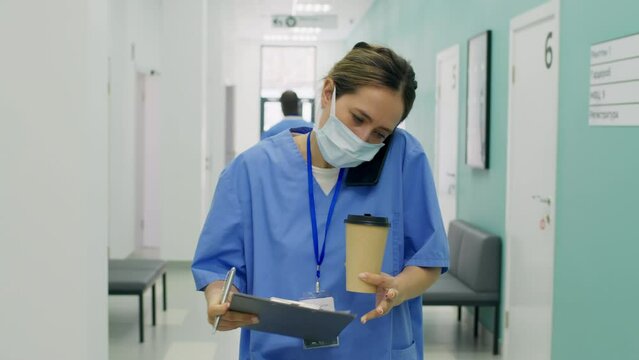 Stressed Nurse Writing On Clip Board While Talking On The Phone