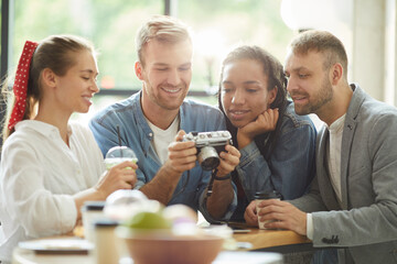 Content young multi-ethnic friends in casual clothing standing at counter in fast food cafe and choosing joint photo on camera screen