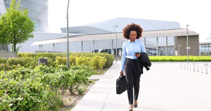 Urban businesswoman with briefcase and smartphone walking on walkway