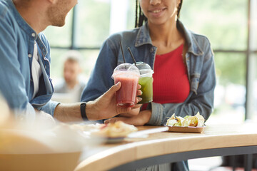 Close-up of multi-ethnic couple standing at counter and drinking healthy smoothie in cafe