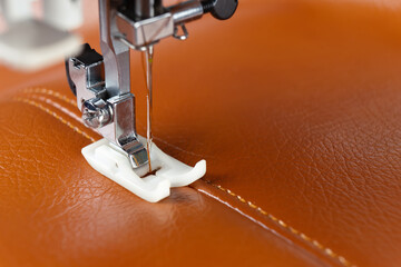 Modern sewing machine presser foot with a needle sews brown leather. Sewing process of decorative...