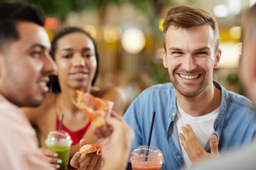 Group of positive young students having communication during lunch: handsome guy haring story to friends and pointing at himself with hand