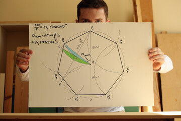 Young mathematician and designer and his drawing regular heptagon with green and blue colours on the paper in hands. Photo was taken 14 May 2022 year, MSK time in Russia.