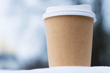 Coffee in a brown paper glass to go in winter outdoors, snow and nature on the background